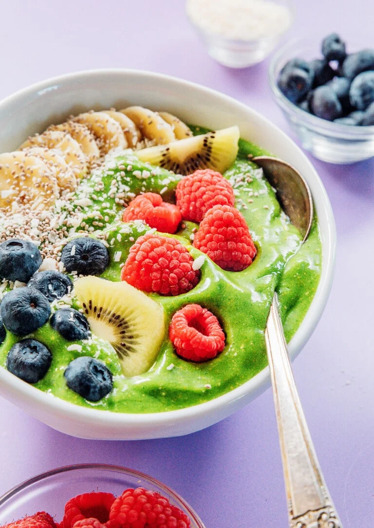 A side shot of a bowl of green smoothie with fruit on top.