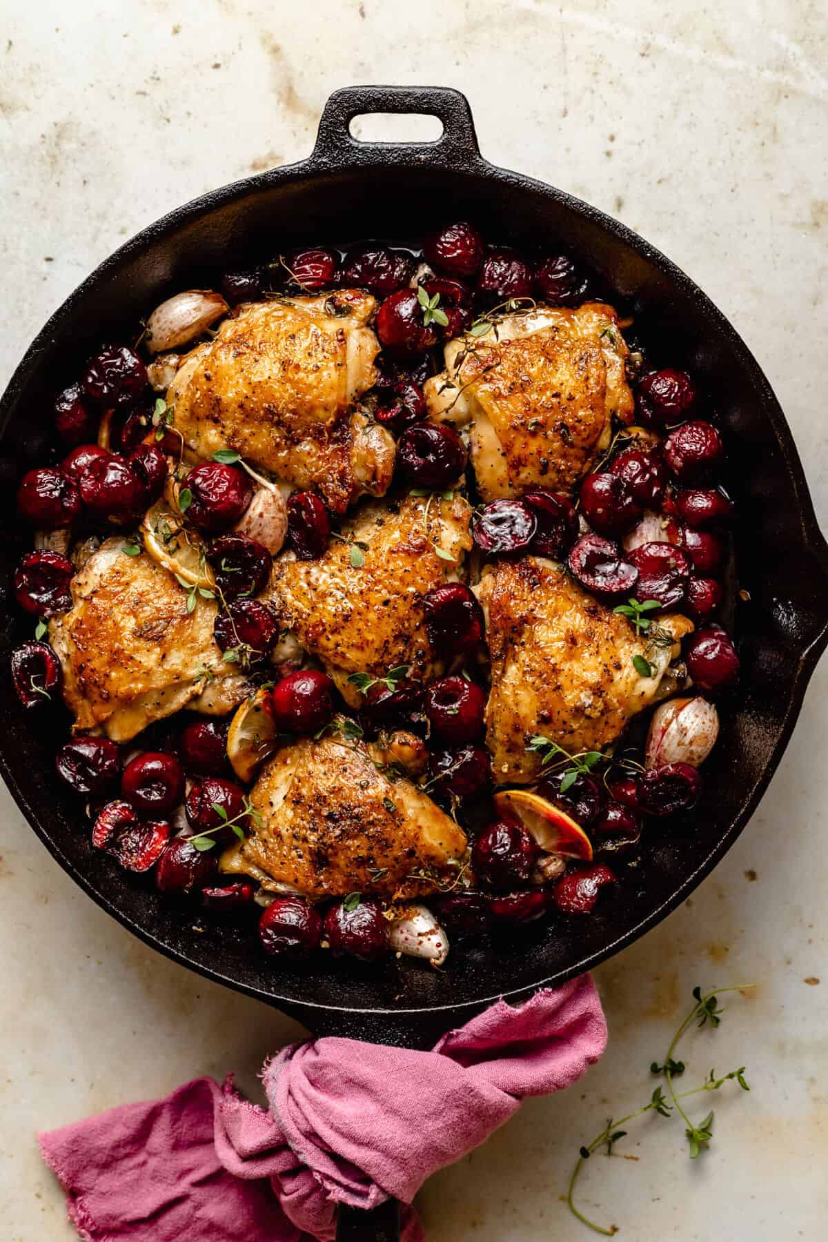 An overhead shot of a cast iron pan with crispy chicken thighs and cherries.