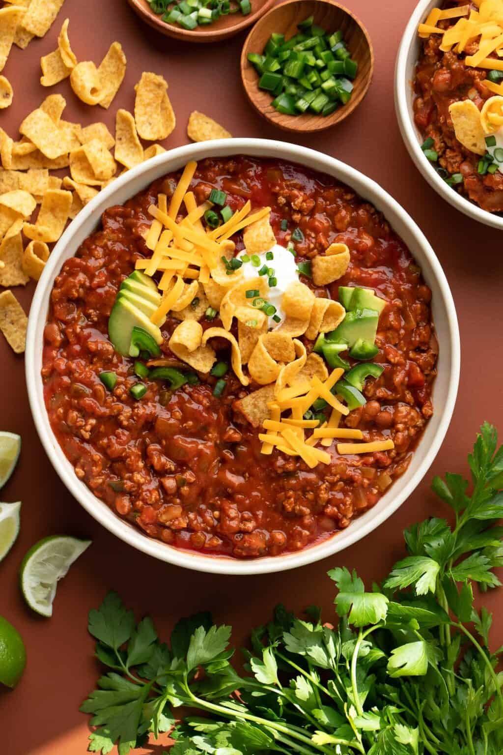An overhead shot of a bowl of turkey chili with toppings surrounding it.