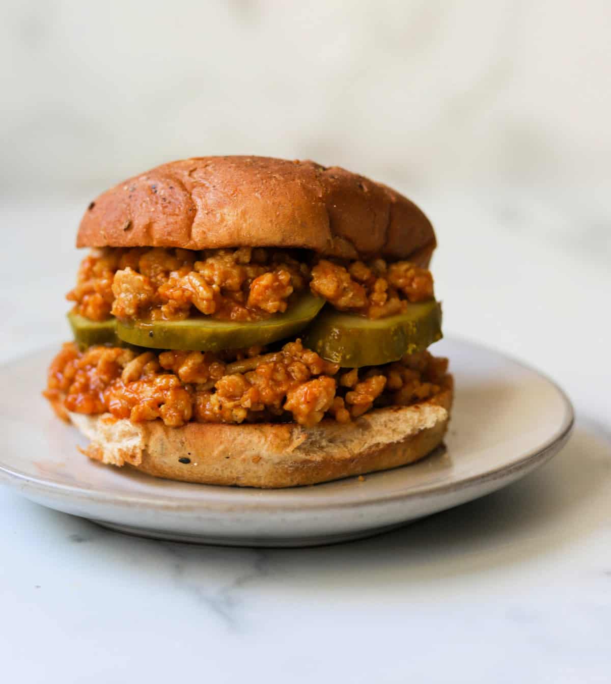 A close up shot of a sloppy joe stacked on a bun with sliced pickles.
