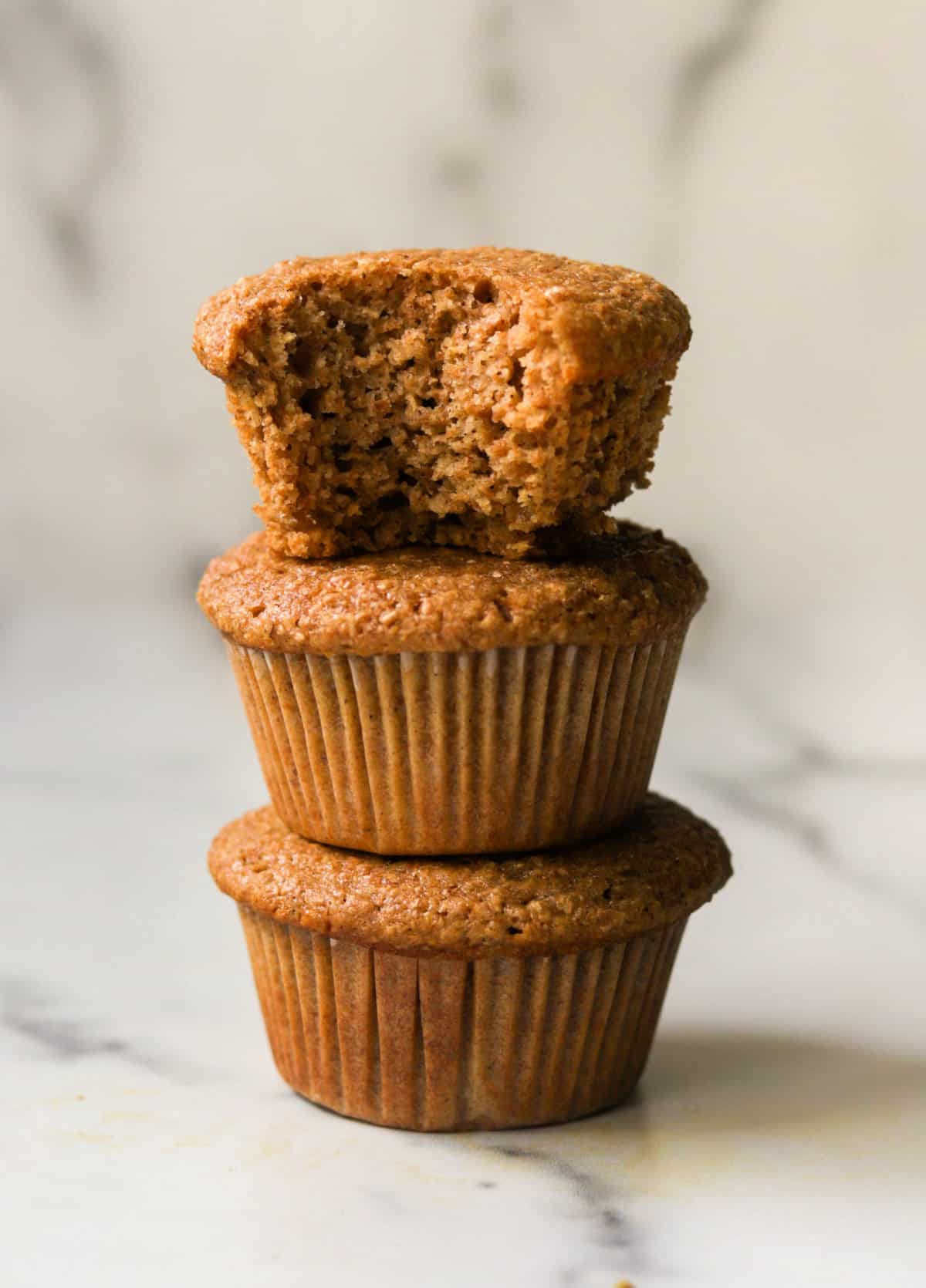 A front shot of bran muffins stacked on top of each other, the top one with a bite taken out of it.