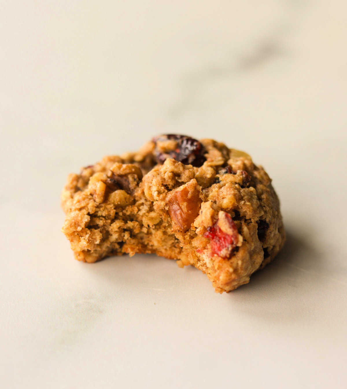 A side shot of an oatmeal cranberry cookie with a bite taken out of it.
