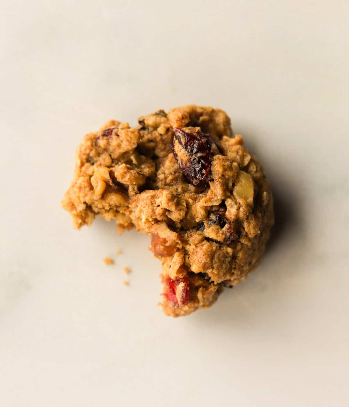 An overhead shot of a single oatmeal cranberry cookie with a bite taken out of it.