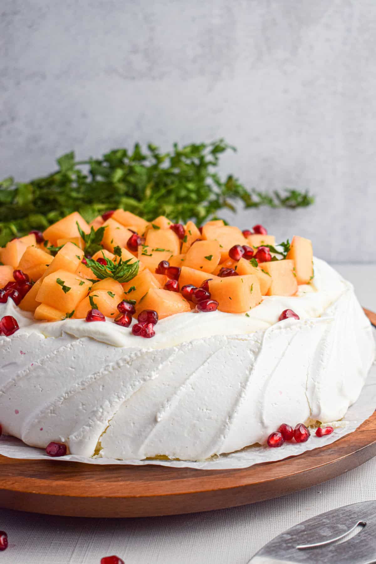 A front shot of a pavlova topped with cantaloupe, herbs and pomegranate.