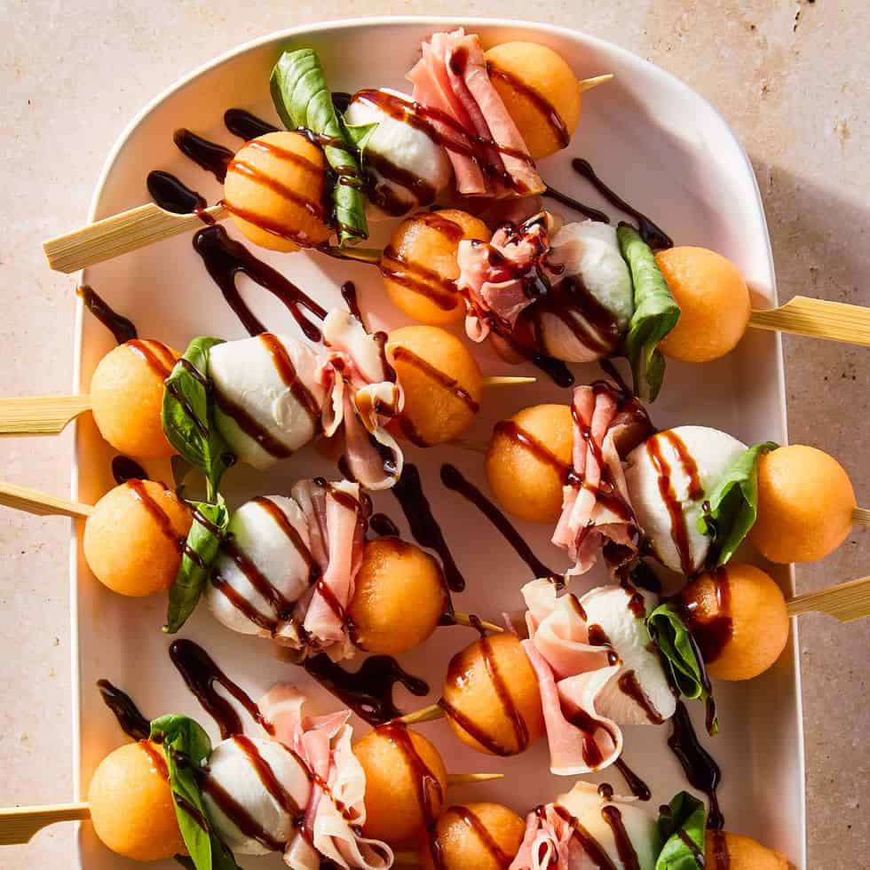 An overhead shot of cantaloupe, mozzarella and prosciutto skewers with balsamic glaze drizzled on top.