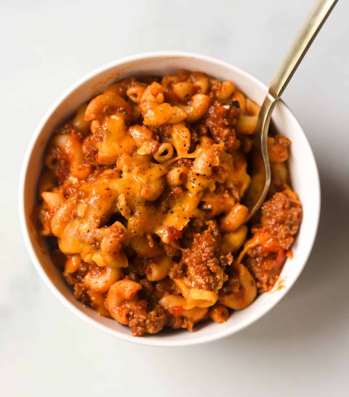 A close up overhead shot of a bowl of cheesy goulash.