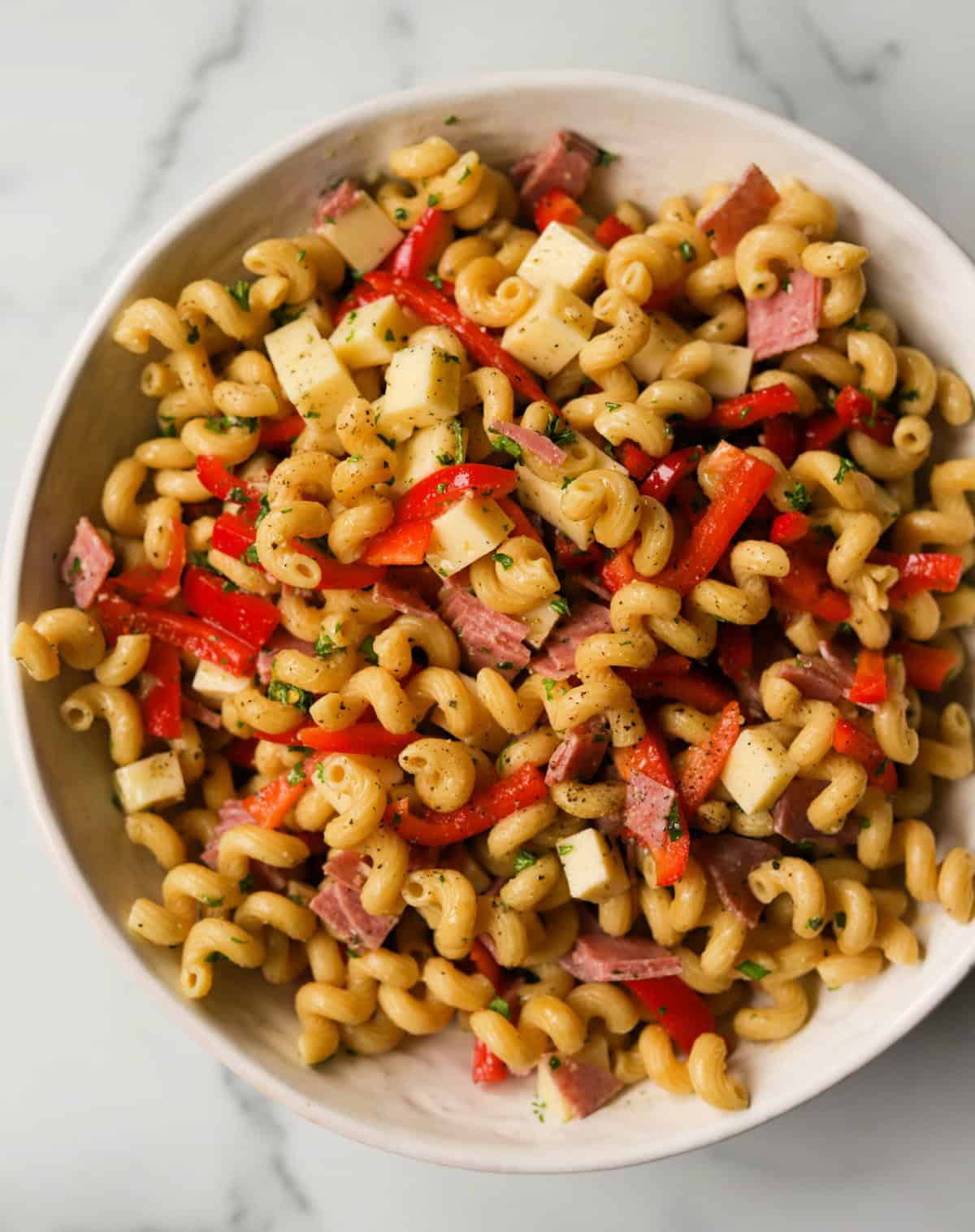 An overhead shot of a white serving bowl filled with Italian cavatappi pasta salad.