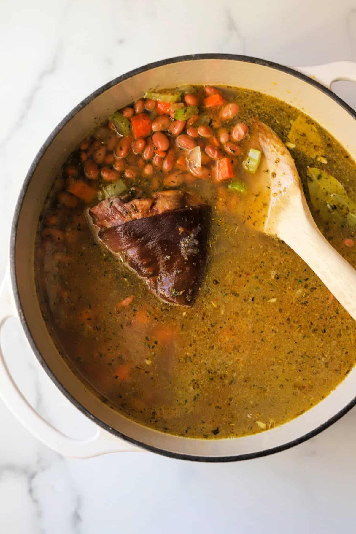 An overhead shot of a pot of pinto bean soup with a ham hock.