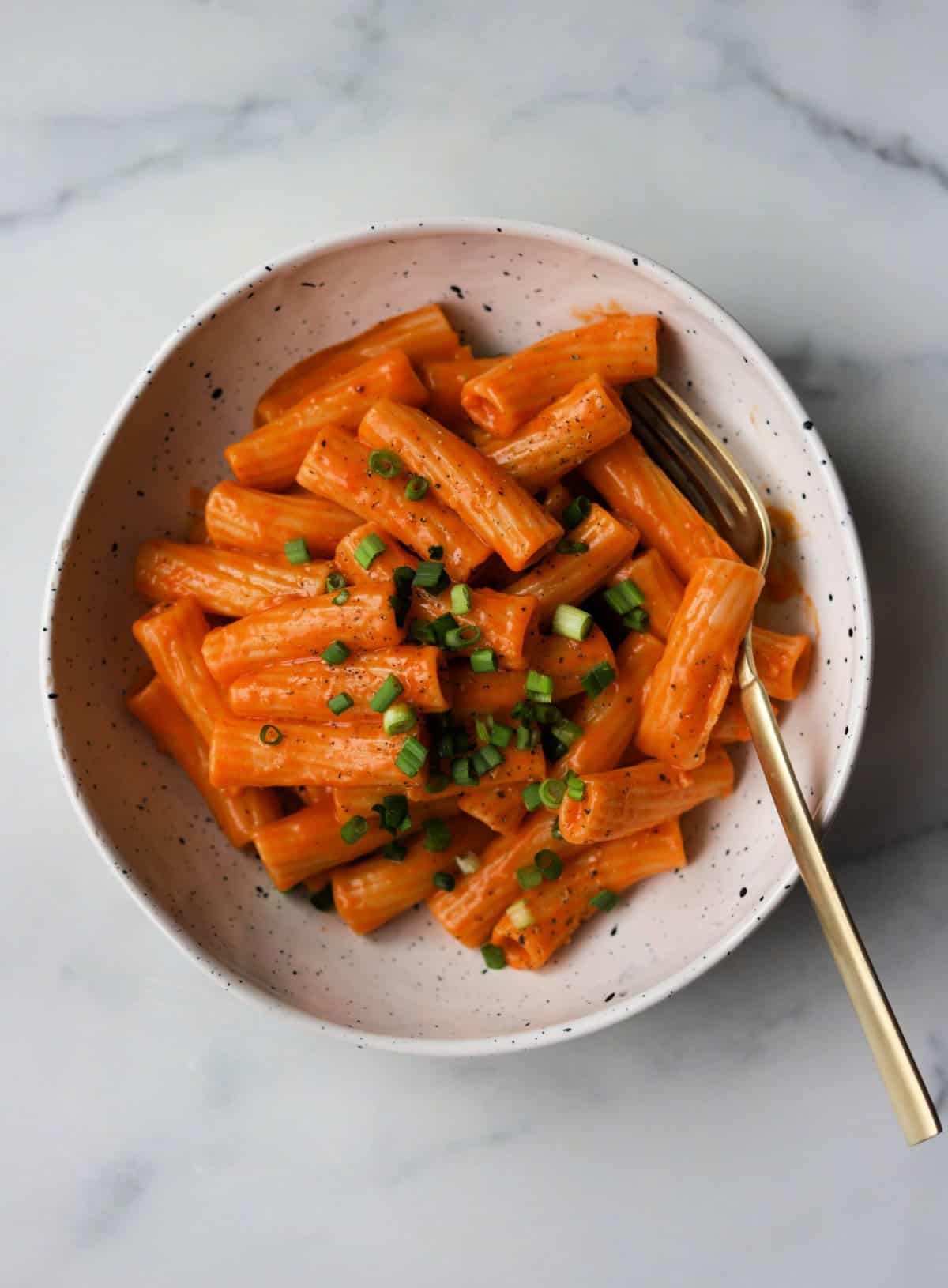 An overhead shot of a bowl of creamy gochujang pasta with green onion sprinkled on top.