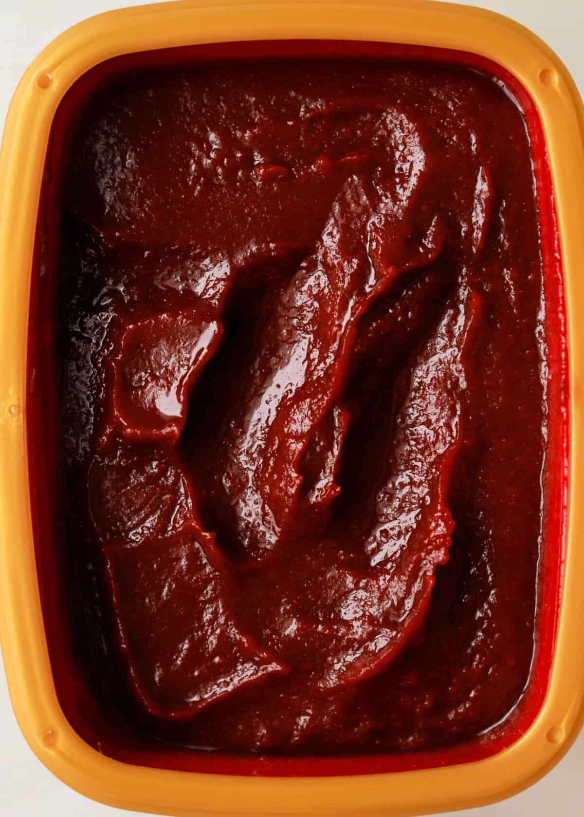 A close-up overhead shot of a tub of gochujang (Korean pepper paste).