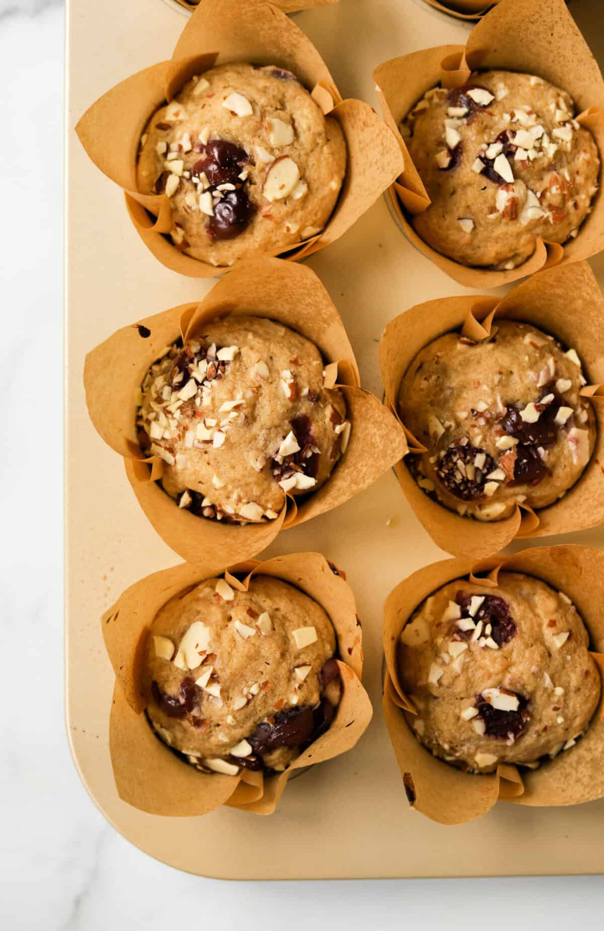 An overhead shot of multiple cherry almond muffins in a muffin tin.