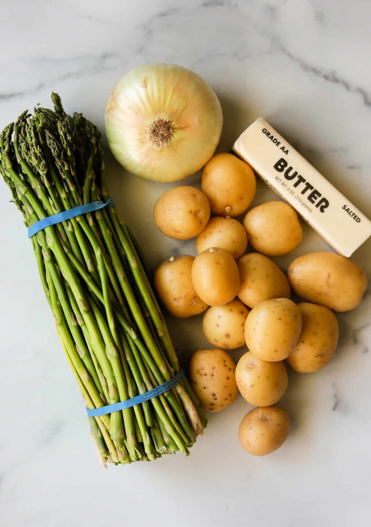 An overhead shot of ingredients for asparagus potato soup on a marble backdrop.