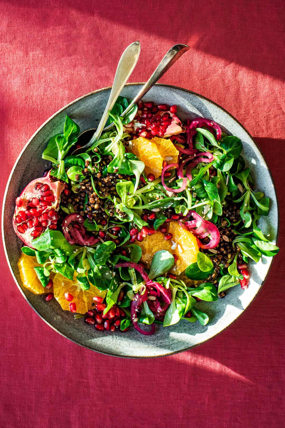 An overhead shot of a green salad with pomegranate, pickled shallots, oranges and crispy lentils.
