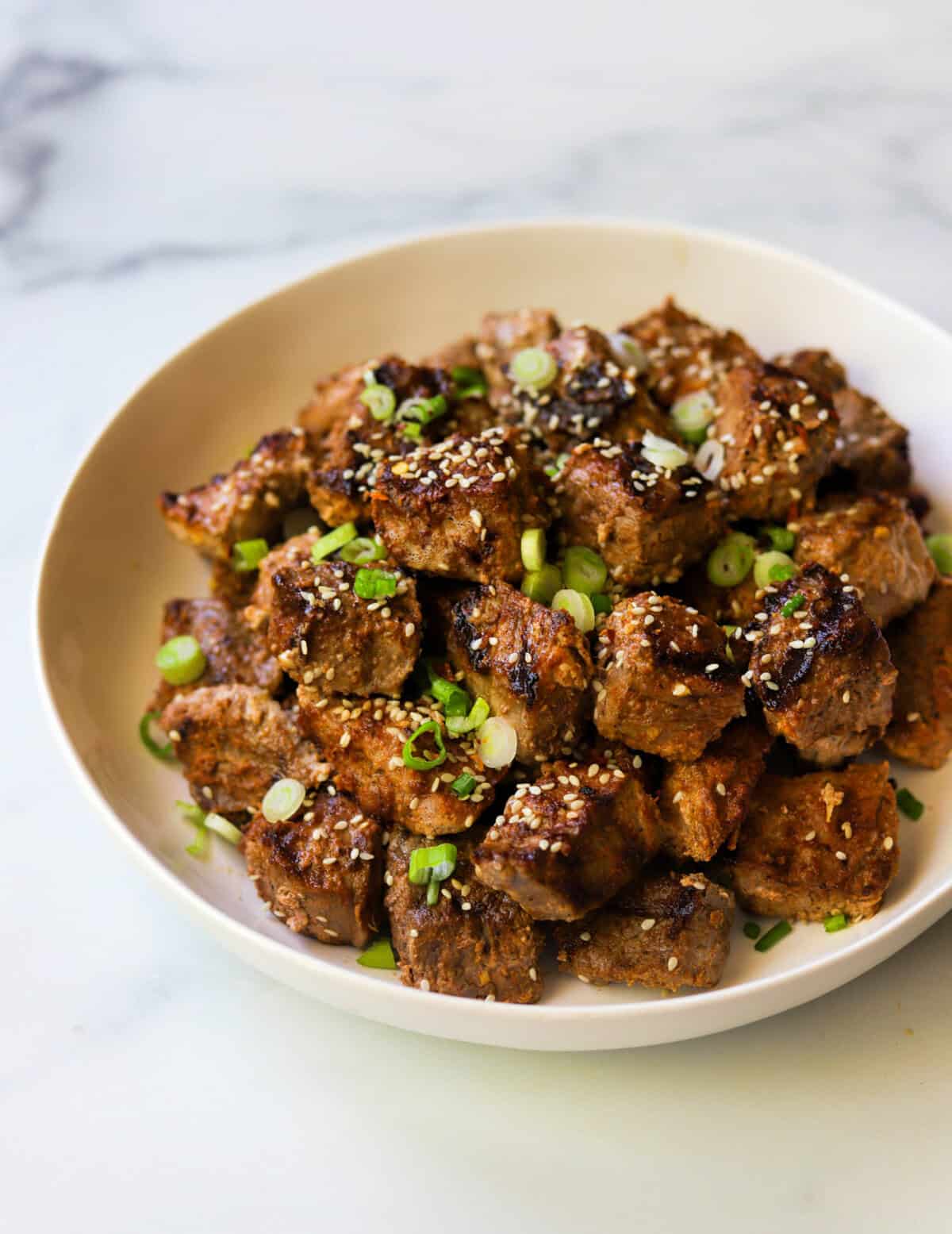 A front angled shot of a platter of grilled steak bites with green onion and sesame seeds.