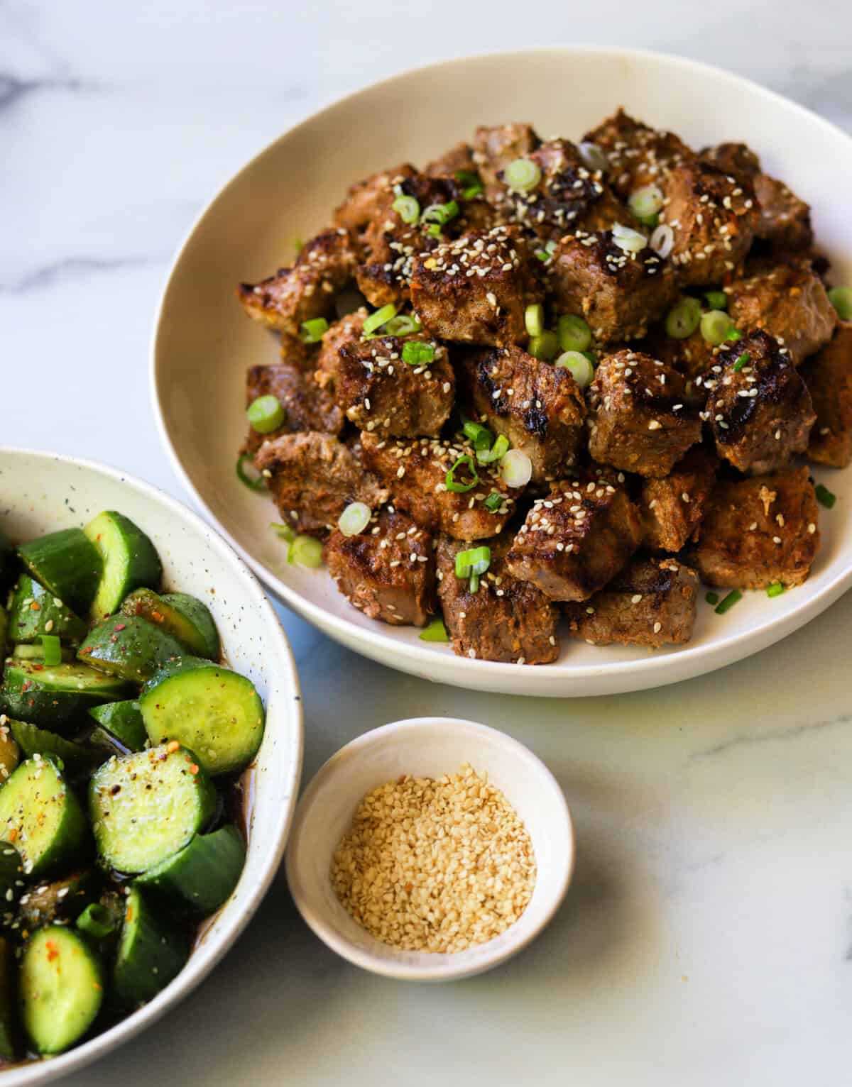 An angled shot of a platter of grilled steak bites with green onion and sesame seeds on top.
