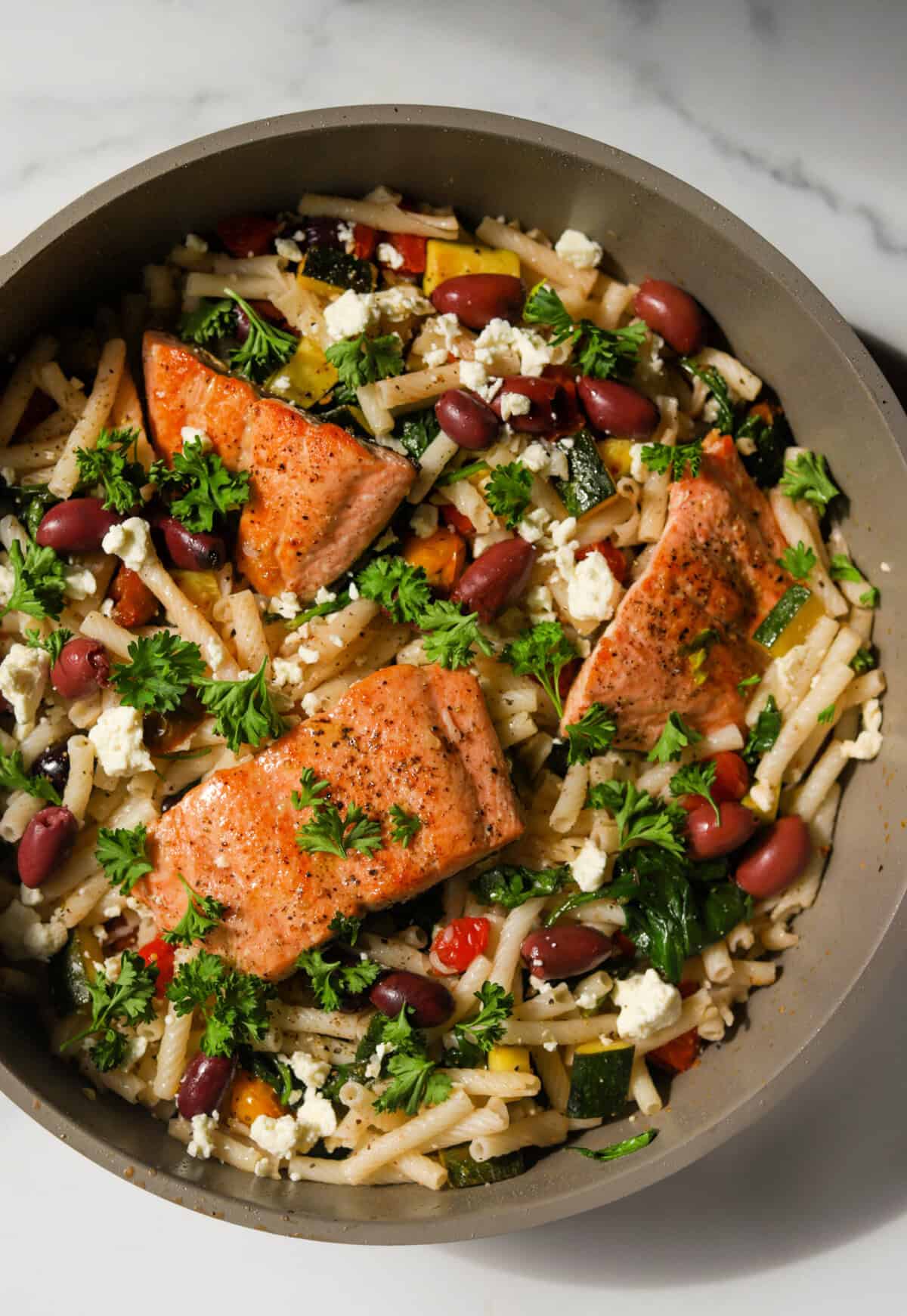 A close-up overhead shot of a pot of lemon pasta with salmon and vegetables.