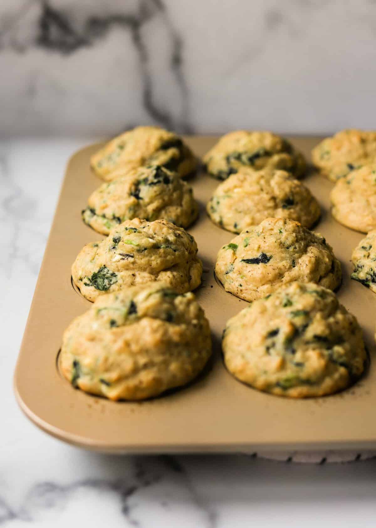 A front angled shot of a gold tin filled with savory spinach feta muffins.
