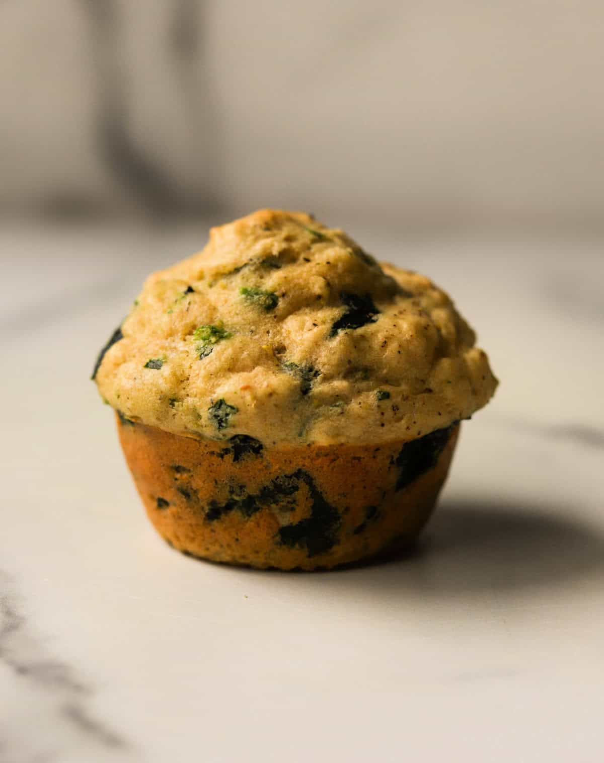 A straight-on front shot of a spinach feta muffin on a white marbled backdrop.