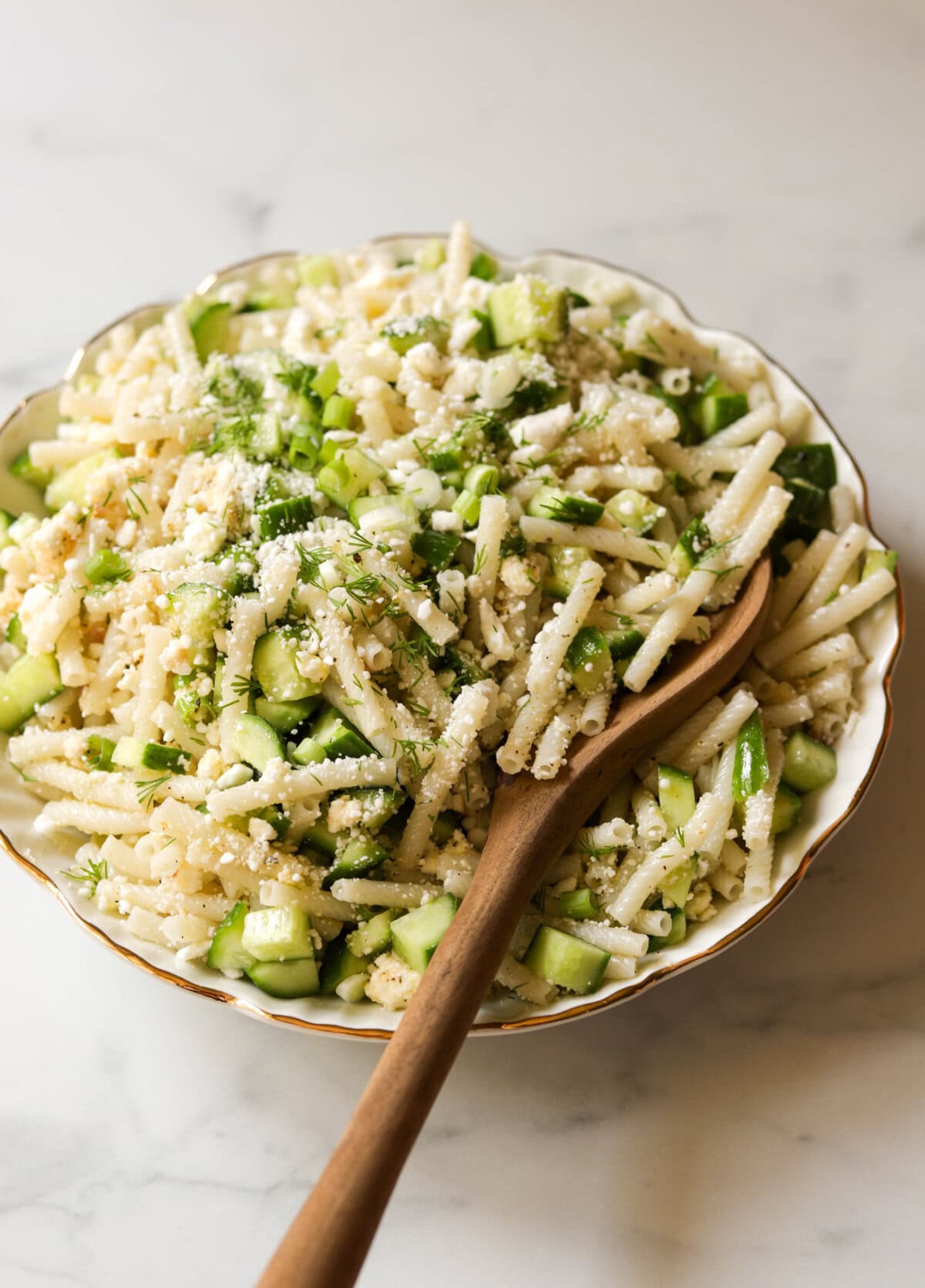 An angled shot of a bowl of cucumber feta pasta salad with fresh dill sprinkled on top.