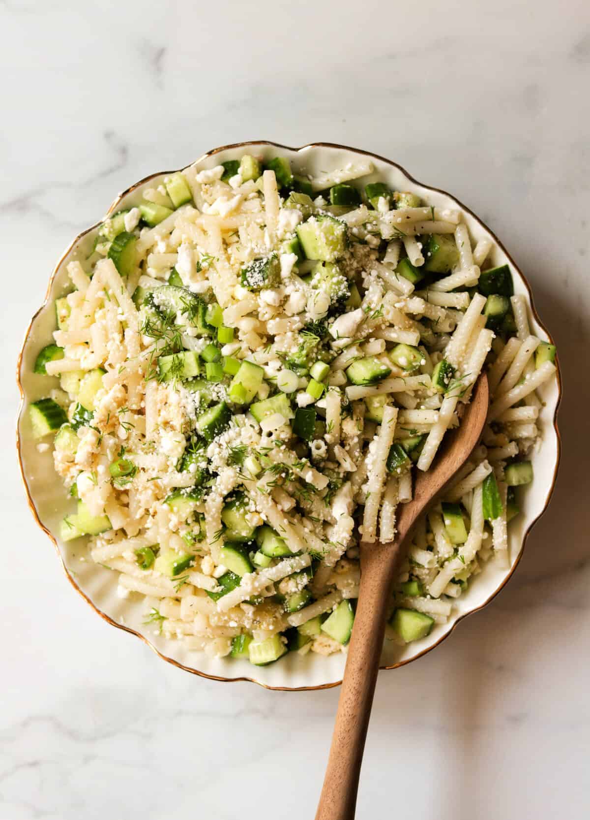 An overhead shot of cucumber feta pasta salad in a white bowl with a gold rim.